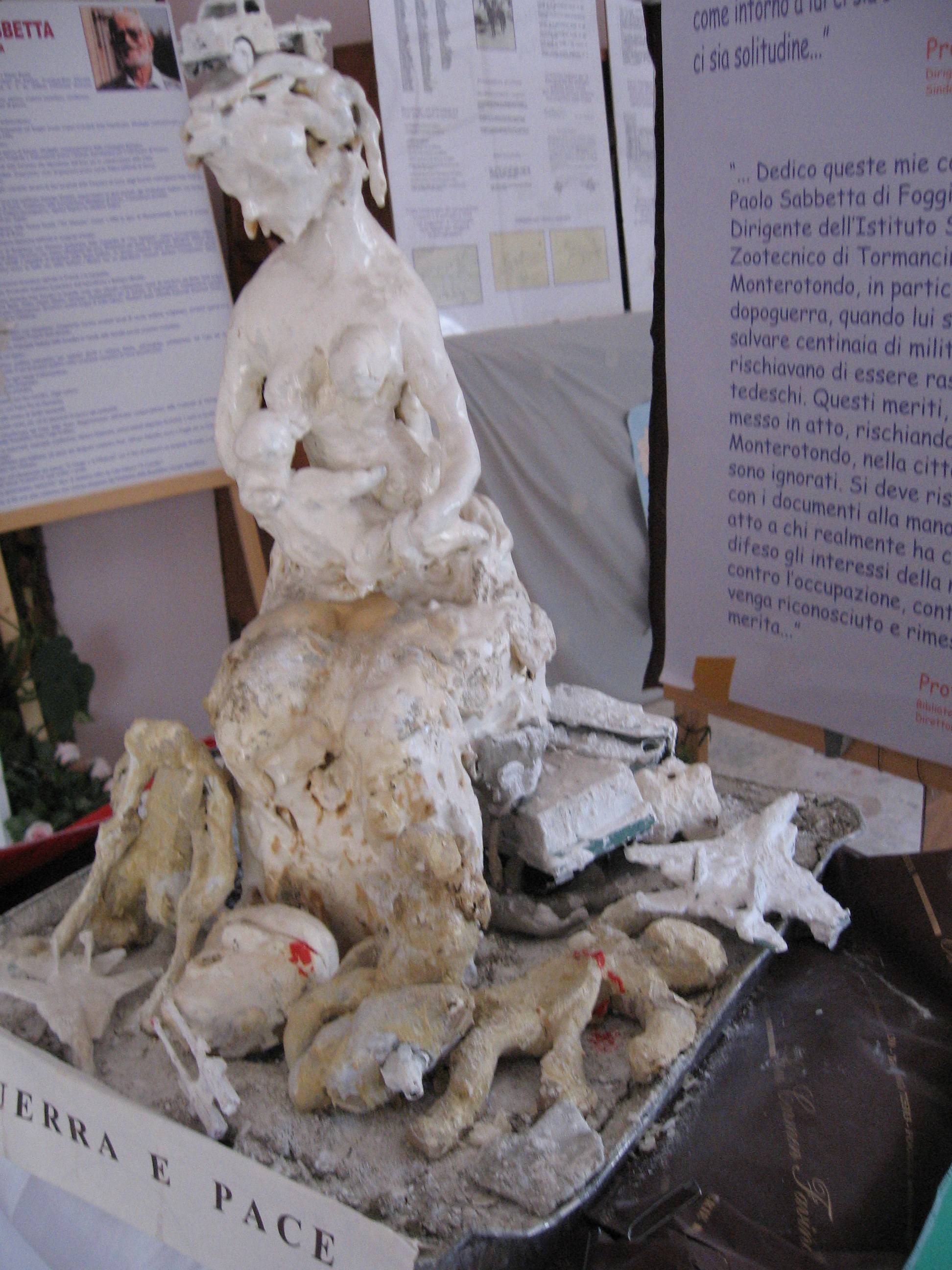 Statua realizzata da Paolo Sabbetta che rappresenta una donna che allatta il suo bambino, simbolo della vita, mentre la guerra ha lasciato distruzione, morte, ferite indelebili e vite segnate. 