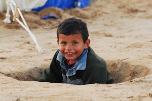 Un bambino gioca in una voragine scavata da una bomba