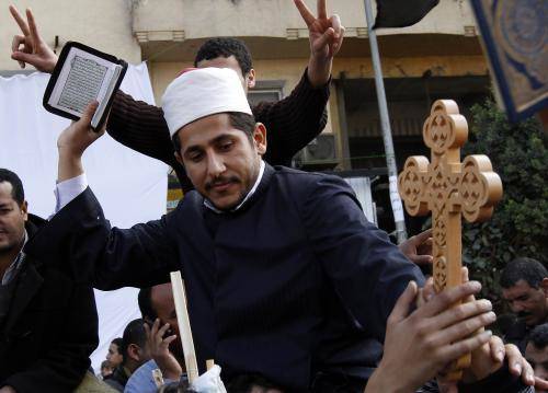 Un religioso musulmano tiene in mano il Corano e una croce Cristiana durante un momento della preghiera comune che si e' svolta al Cairo