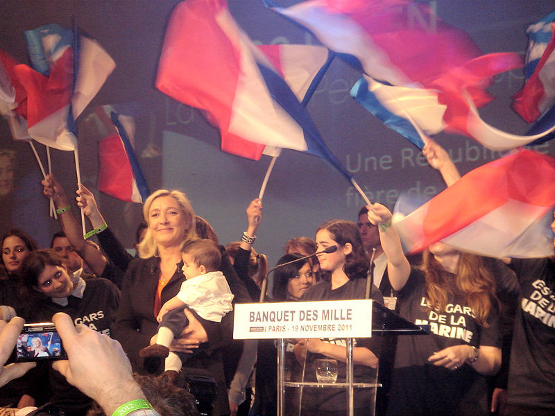 "Marine Le Pen, bébé, drapeaux, banquet des Mille3louis maitrier" di NdFrayssinet - Opera propria. Con licenza CC BY-SA 3.0 tramite Wikimedia Commons 