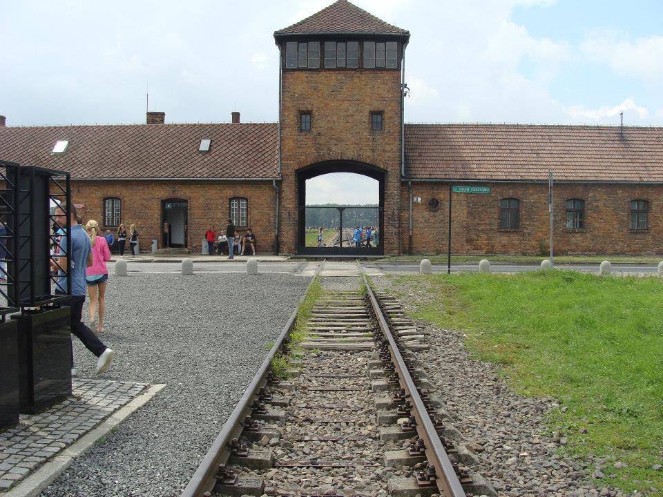 Ingresso del campo di sterminio di Birkenau, con immagine in primo piano delle rotaie che conducono al suo interno. 