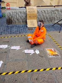 In piazza de Ferrari a Genova, un attivista con la maschera di Julian Assange si siede in una “cella” tre metri per due disegnata sul pavimento con il nastro adesivo.