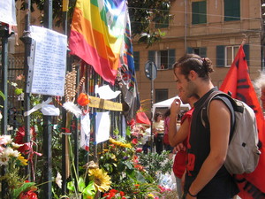 Genova, 20 luglio 2004, piazza Alimonda. Un gruppo di ragazzi osserva l'"altare laico" fatto di fiori e bigliettini lasciati sulla cancellata della chiesa di Nostra Signora del Rimedio.