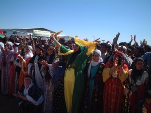 Nello spiazzo antistante il palco, una folta schiera di donne e ragazza vestite con abiti tradizionali curdi