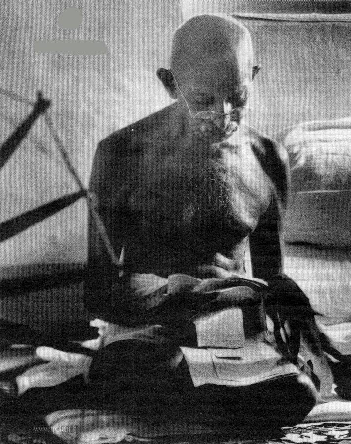 Foto di Gandhi che legge seduto sul pavimento.