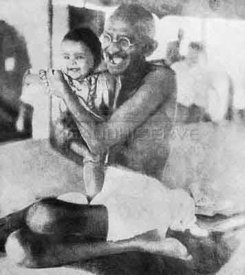 Gandhi seduto ride con un bambino in braccio