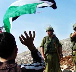 Bambino palestinese che sventola una bandiera di fronte ad un soldato israeliano.